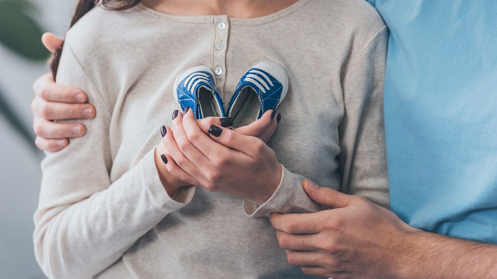 Hände halten ein paar Kinderschühchen und drücken sie an den Oberkörper: Umgang mit der Trauer | Bild: colourbox.com