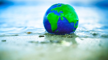 Erdkugel im Wasser; nicht nur beim Duschen verbrauchen wir Wasser, auch beim Konsum lohnt der Blick aufs virtuelle Wasserkonto. | Bild: picture alliance | Christian Ohde